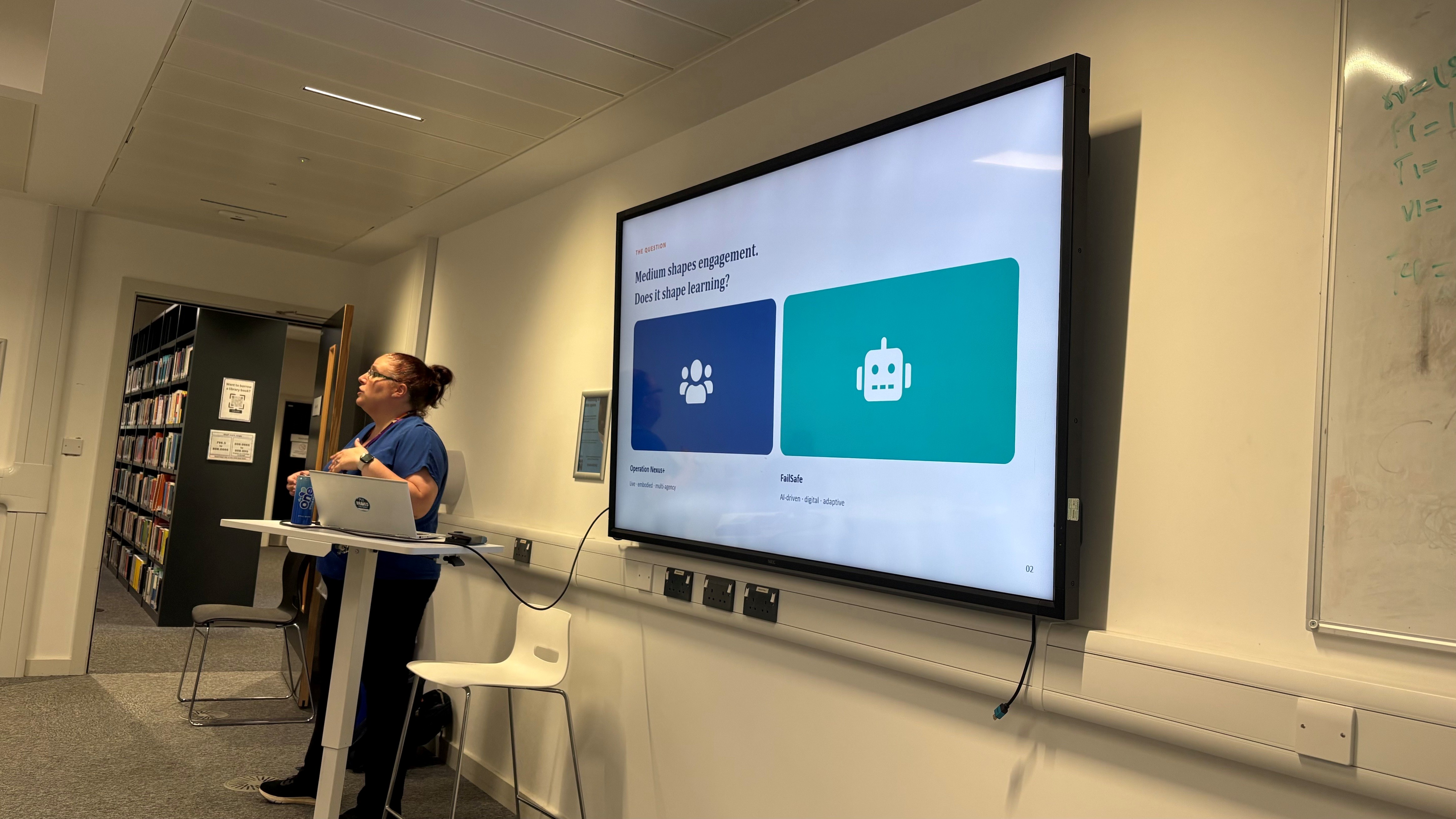 Person doing a presentation in front of a screen. The screen has two buttons, one dark blue with an icon of people and another light blue with a android robot icon.