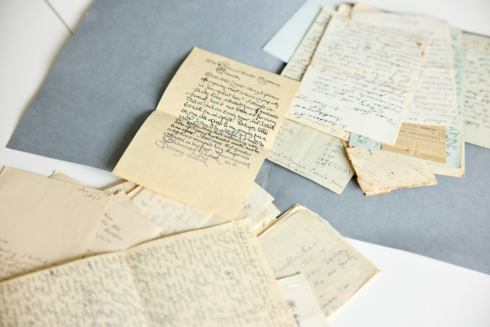 Pile of handwritten letters on a table, various paper types and handwriting indicating they are historical.