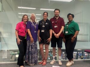 Five Nursing course academics stand in front of a glass wall in a Learning Hub classroom.