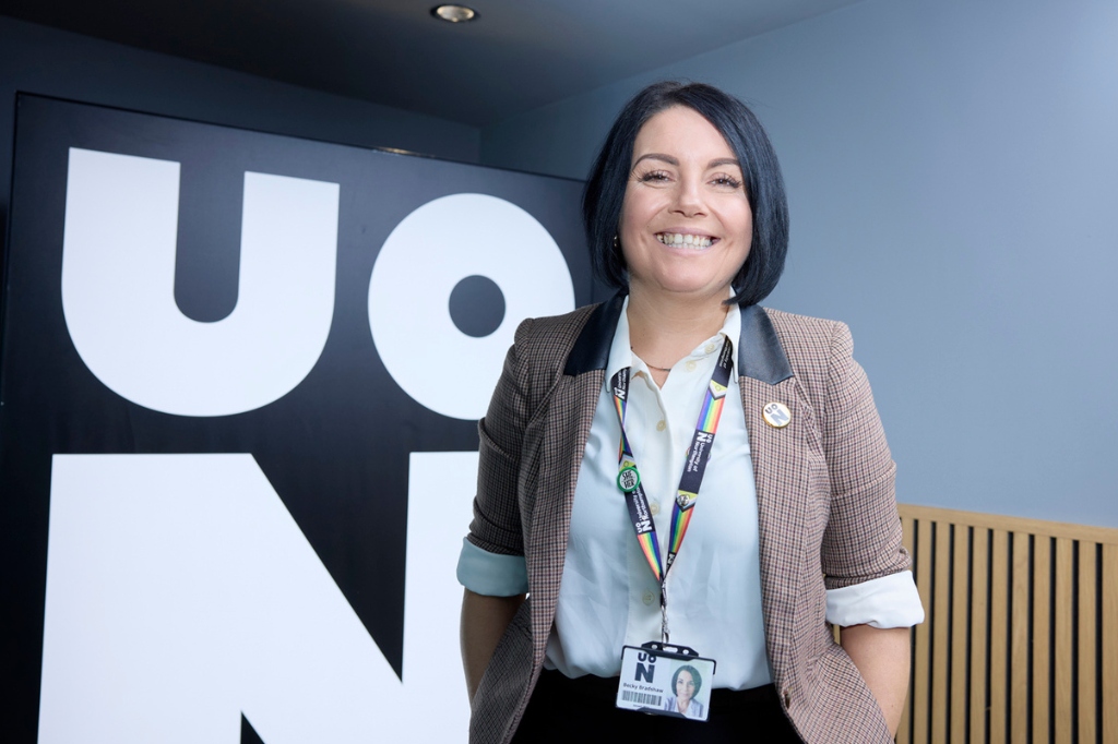Becky Bradshaw smiles at camera with 'UON' illuminated behind her.