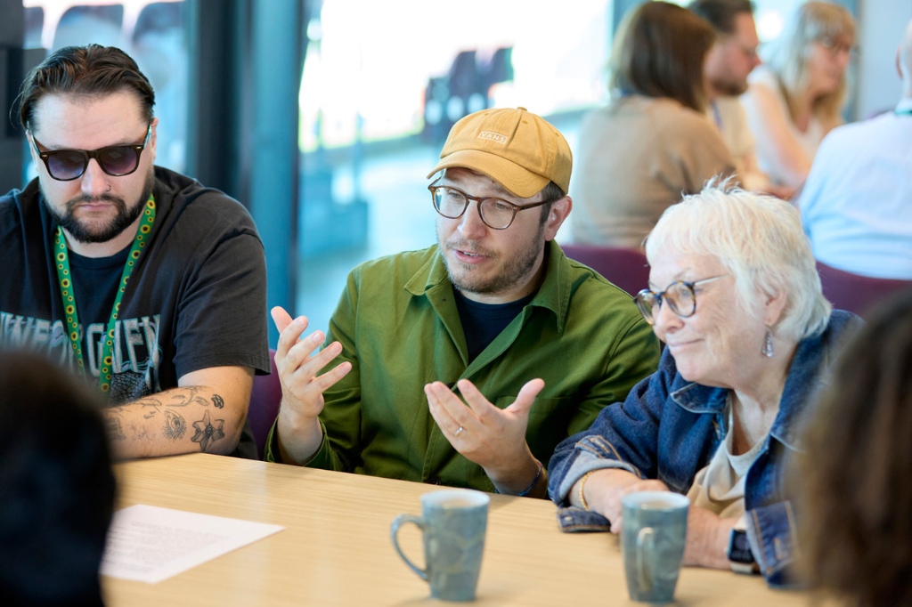 Three people talk in conversation at a table discussion.