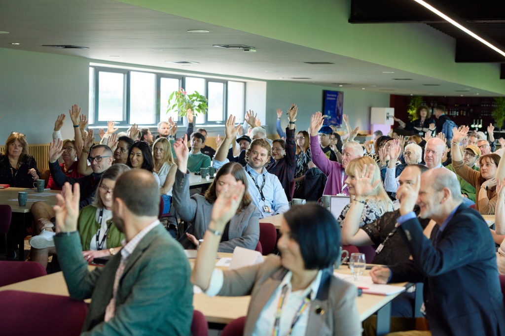 Group of people in meeting have their hands raised and smiling.