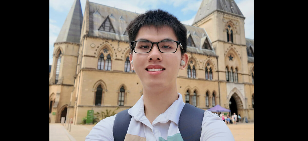 Chi Cuong Tran, standing in front of a big, old castle style building with large roofs and windows.