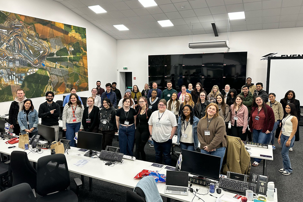 Photo of over 40 people in a room, standing behind desks with laptops and notepads, looking at the camera and smiling for a group photo.
