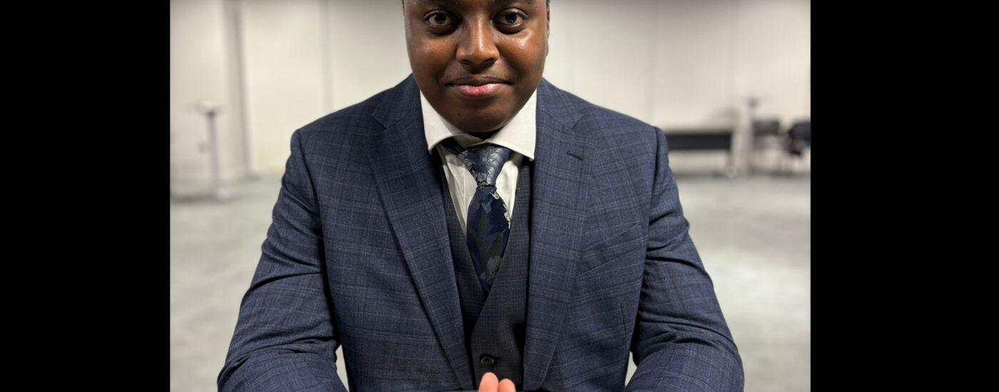 Ryan Gichuru, wearing a suit and sitting in front of the camera, smiling