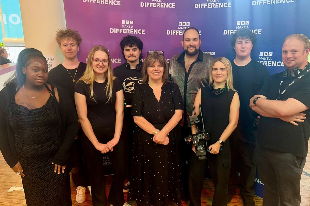 Group of people smile in front of camera in front of a 'BBC Make A Difference' award sign.