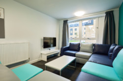 Communal area of Student Village, showing a corner sofa which can fit approximately 8 people and a TV on the wall.