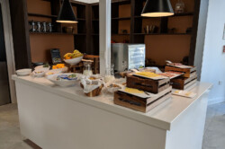 Sunley Hotel breakfast bar, showing a toaster oven, trays of meat and cheese, bowls of yoghurt and fruit, and jugs of milk.