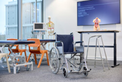 A wheelchair in the Physiotherapy Laboratory classroom, which a desk behind that has a skeleton model.