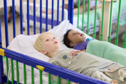 Two child manikins next to each other in a crib ward bed, in the Simulation Lab
