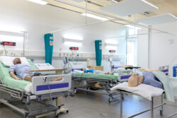 4 Manikins in the Simulation Lab, each on a ward bed with wires connected to them. Two have oxygen masks on their faces. There are digital clocks above the beds.