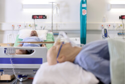Two manikins in the Simulation Lab one is close to the camera and blurred, but an oxygen mask can be seen. In the background is another in a ward bed.