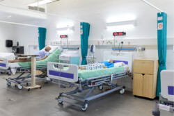 Real experience ward in the Simulation Lab, showing two patient manikins in bed, with curtains, wires, bedside tables, and movable beds. There is a digital clock above each bed.