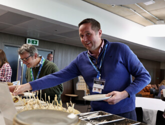 Photo of three delegates getting food from the breakfast table buffet at the UON Sustainability Summit 2023. The guest in the middle is looking at the camera and smiling.