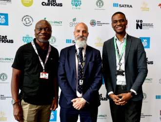 3 people at the UON Sustainability Summit 2023 standing in front of a board full of sponsor logos. On the right of the group is Dr Ebenezer Laryea Associate Professor and Chair of the Planning Committee UON Sustainability Summit.