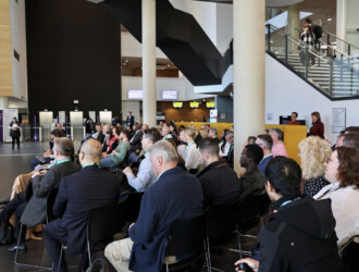 Approximately 40 delegates sitting in rows and booths at the UON Sustainability Summit 2023. They are looking in one direction presumably towards a speaker.