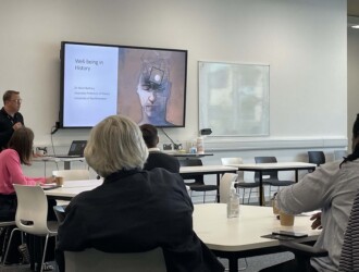 Professor Mark Rothery introduces a presentation on wellbeing in history in a University of Northampton classroom with a digital screen on the wall displaying slides