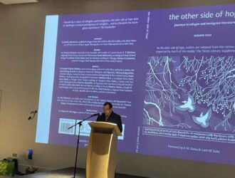 PhD candidate Amir Darwish stands at a lectern in front of a large digital screen displaying a slide entitled 'The other side of hope'