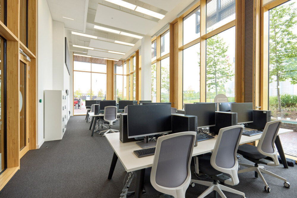 Internal view of the Bloomberg Finance Lab at the University of Northampton. There are desks of 6 desktop computers with desk chairs, filling the room which has big ceiling to floor windows.