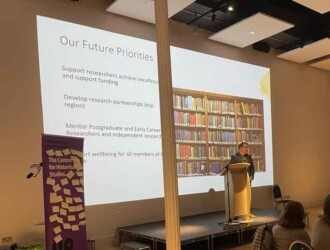Professor Mark Rothery stands in front of a large digital screen addressing an audience about future priorities for the Centre for Historical Studies