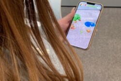 A person is holding a smartphone in one hand - with the phone screen clearly visible. Extended reality figures appear on a smartphone screen