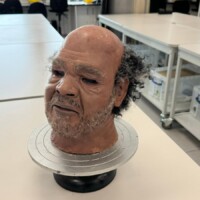 Pictured on a stand is the clinical simulation mask created by Poppy Twigger for use in Occupational Therapy teaching and learning sessions.