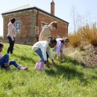 An image of children wearing wellington boots and searching in the grass for something at the Forest School.