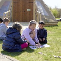 A photo of Forest School children gathered round stones outside the tipi.
