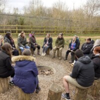 A team sat on logs and gathered in a circle discussing activities.