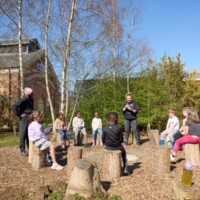 Photo of a group of children sat round on logs with a group leader.