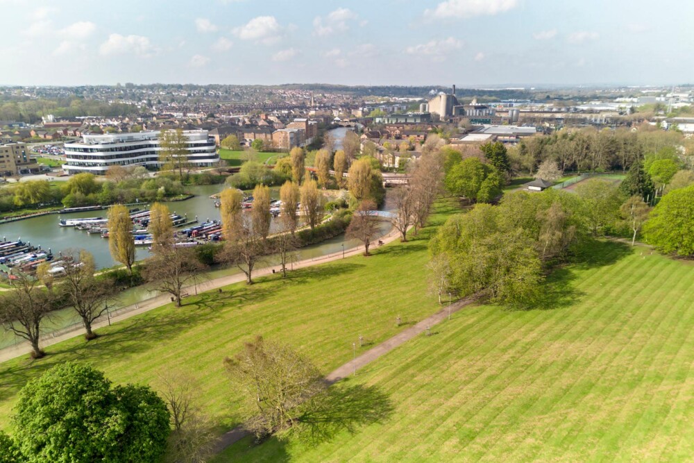 Aerial view of Becket’s Park’s grass areas, trees and footpaths. In the background, there are many boats moored in Northampton Marina, and the curved white Creative Hub building on Waterside campus.