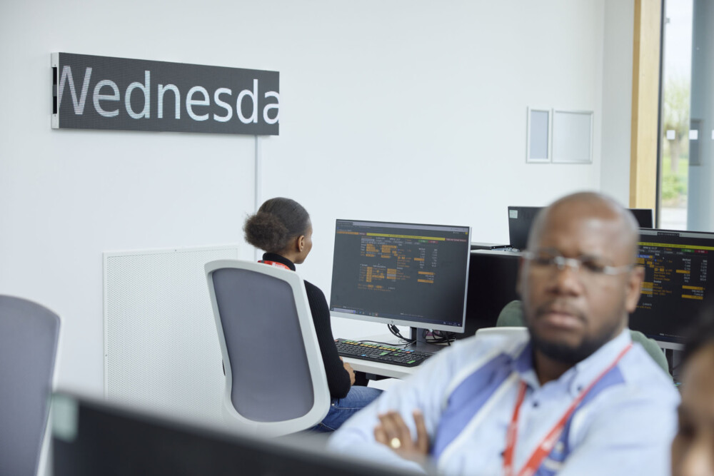 Two students working on terminals in the Bloomberg Finance Lab. They are seated near a moving screen that is mounted on the wall
