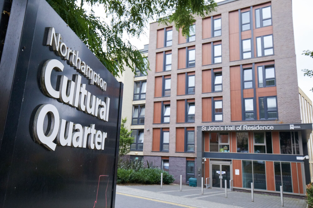 Entrance to St John's Hall of Residence, a brick building of several storeys with large windows. In the foreground, there is a large place sign that reads ‘Northampton Cultural Quarter’.