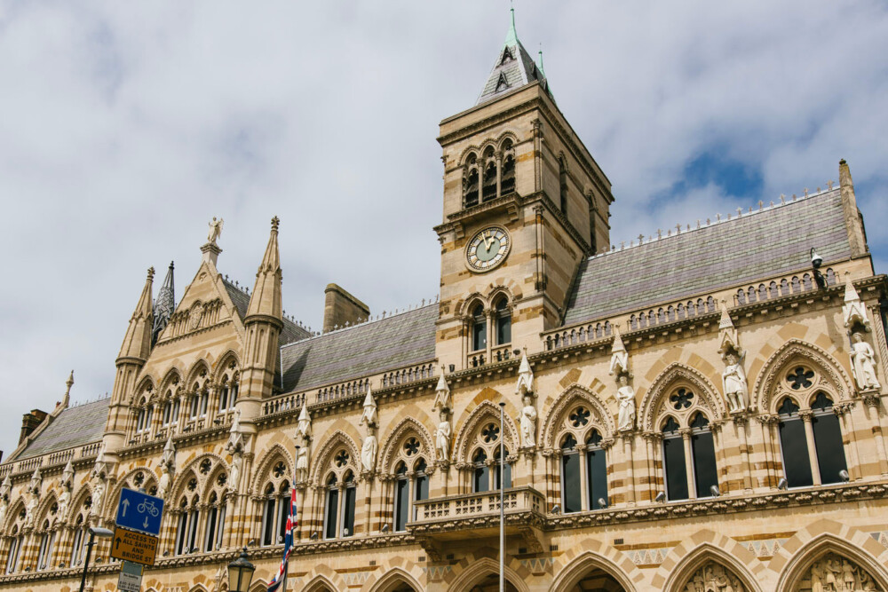 Gothic-style building with arched windows and a clock tower under a cloudy sky.