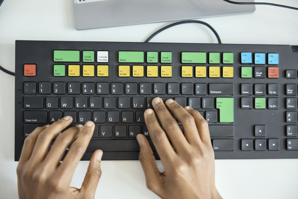 A pair of hands on a specialist Bloomberg keyboard, which is made up of red, green, white, blue and black keys.