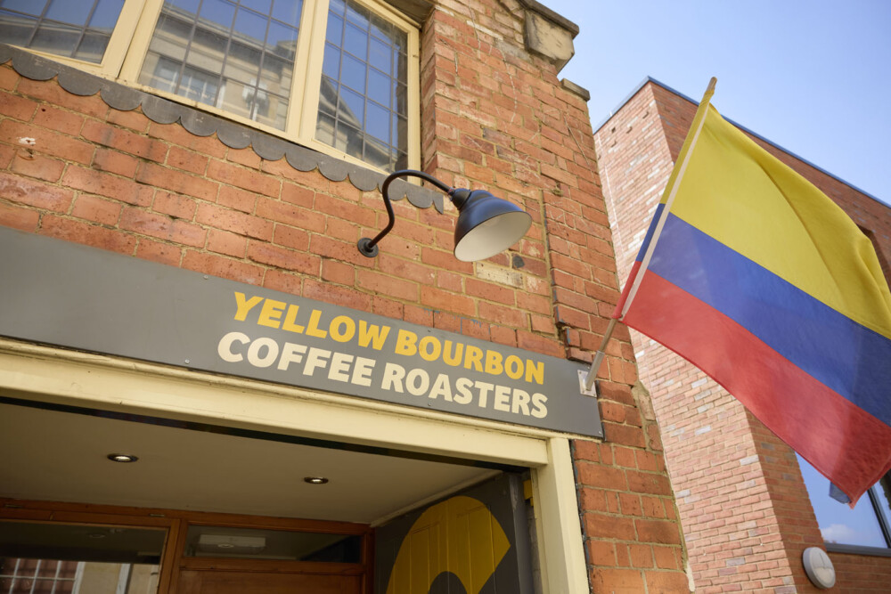 Close up of the Yellow Bourbon Coffee Roasters sign with a Colombian flag of yellow, blue, and red stripes hanging outside the entrance.