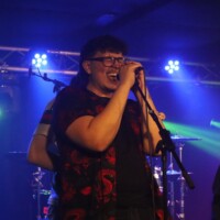 Person singing passionately on stage with colorful lights in the background.