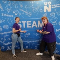 two members of UON staff are pictured in front of the STEAM Northants logo.