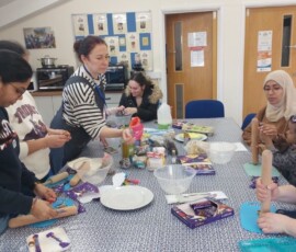 A group in a cookery class sat round a table using rolling pins to crush food.