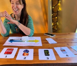 A person sat at a wooden table with four cards on the side ranking sugar in well known drinks from worst to best.