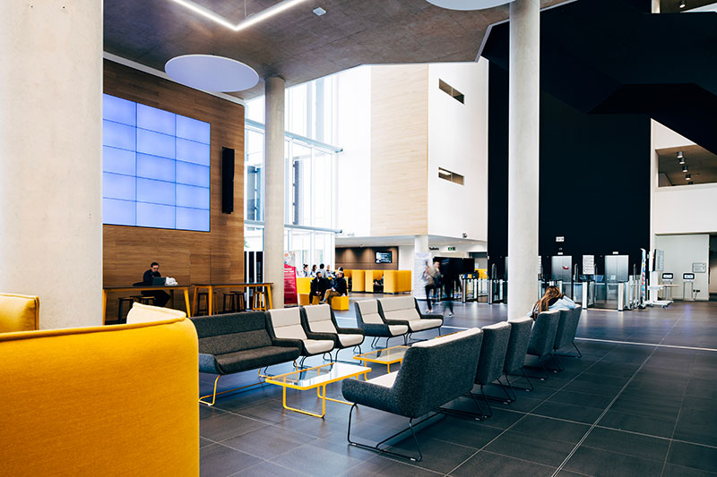 Seating area in front of the big electronic screen in the Learning Hub foyer, at the University of Northampton.