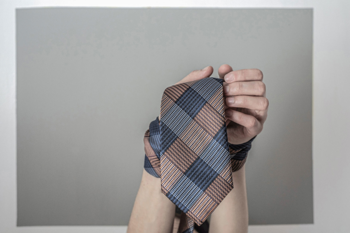 Image of two hands with a coloured striped tie wrapped around them