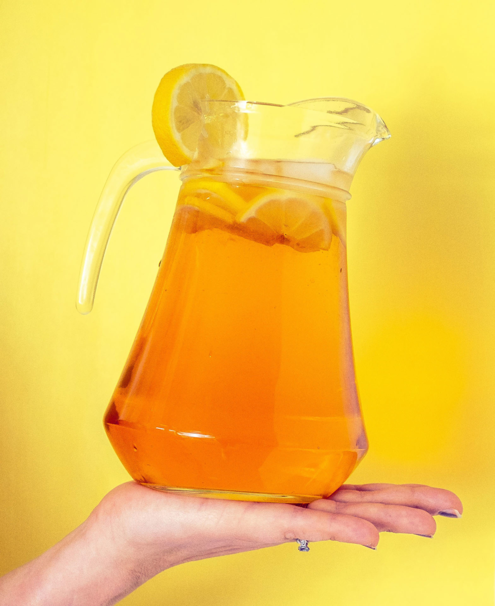 image of a hand balancing a glass jug, the jug is filled with a light brown liquid.