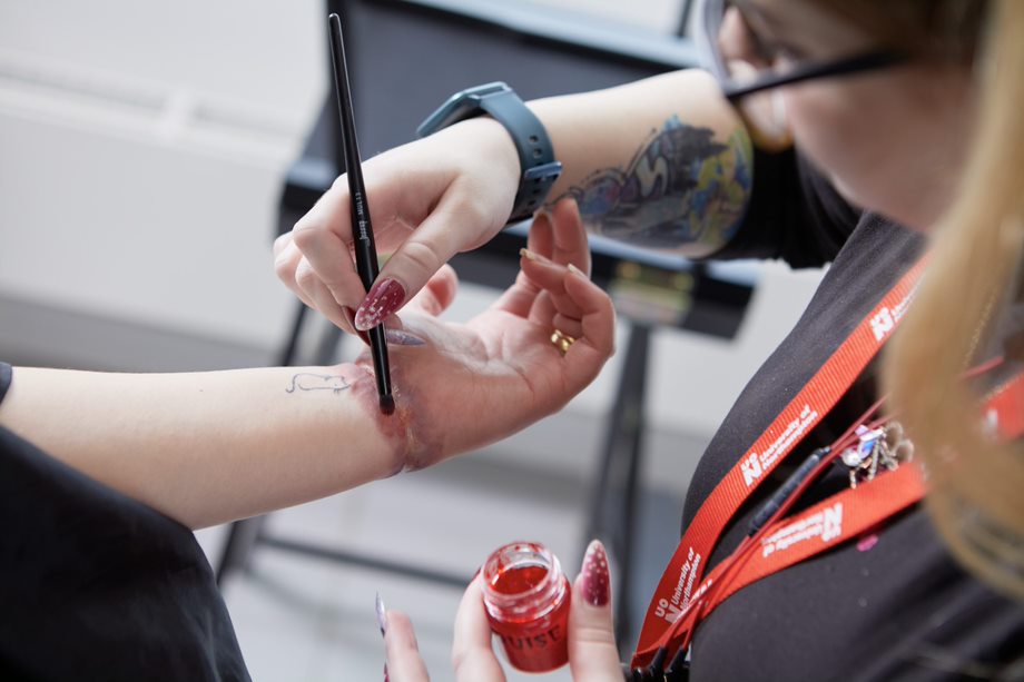 Student applying make-up to wrist with paintbrush
