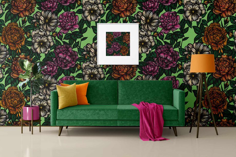 A room with floral wallpaper, a green sofa with orange cushions and an orange lamp