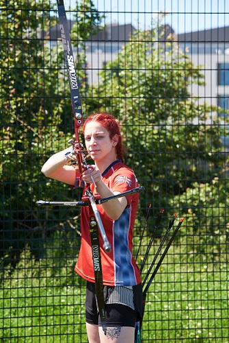 Female student holding an archery bow, which is pointed at the camera